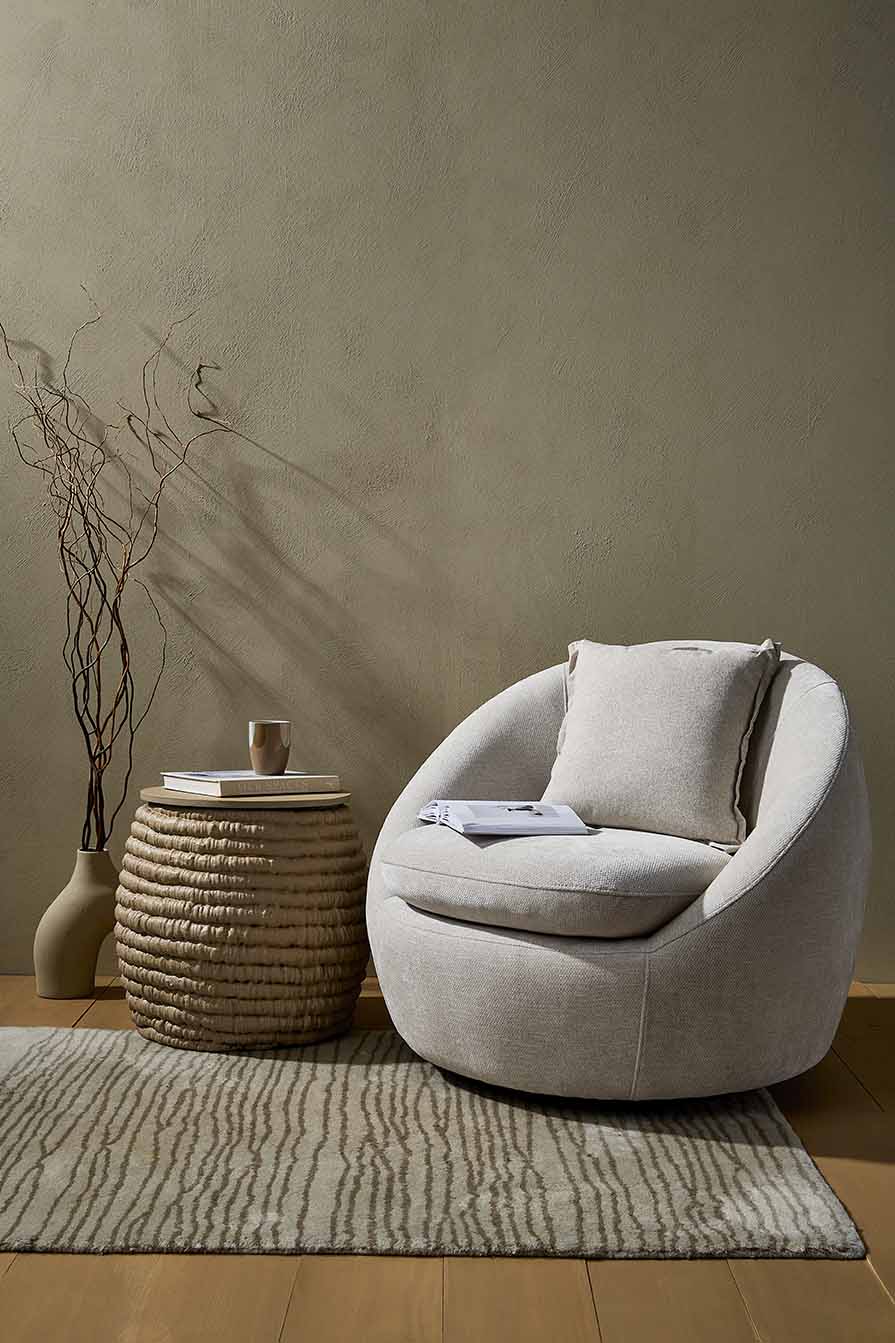 Full room view — rounded chair, rug and curly branch vase against textured wall